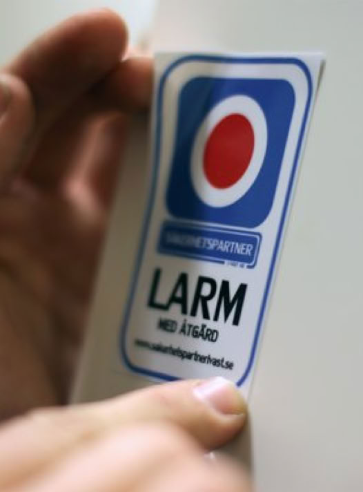 A hand holding a sticker with a blue and red circular design and text in Swedish.