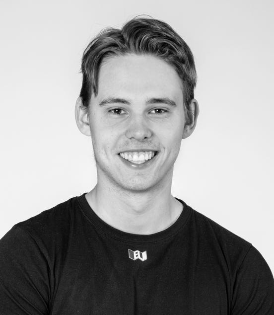A black and white portrait of a smiling person with short hair, wearing a dark shirt.
