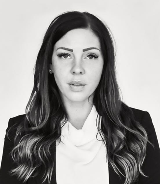 Black and white portrait of a woman with long hair, wearing a dark blazer and a light-colored blouse, looking directly at the camera.