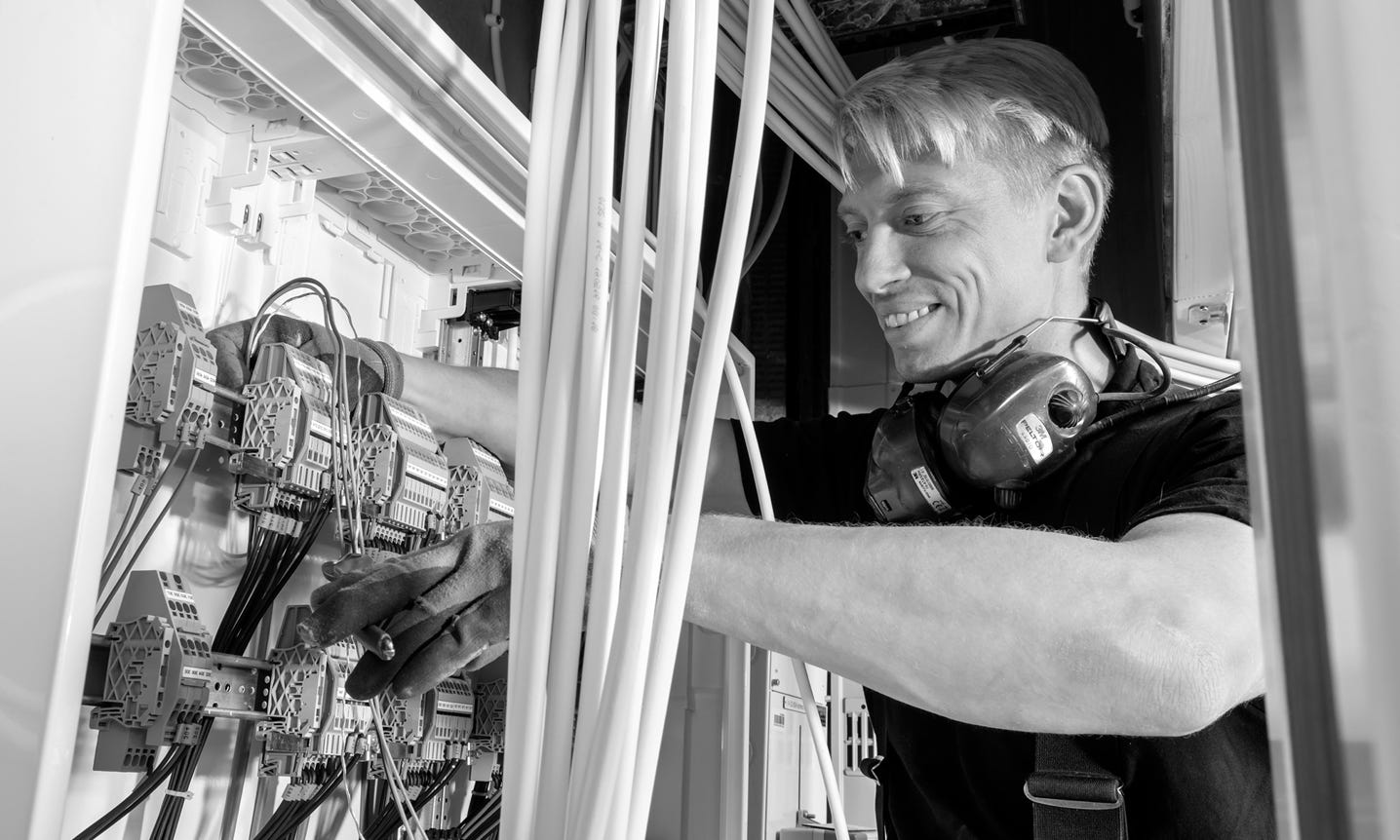 Person working on electrical wiring in a panel, wearing headphones around their neck.
