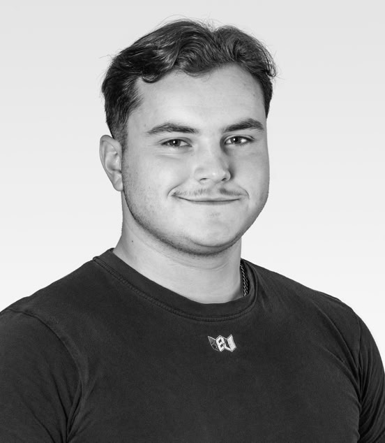 A black and white portrait of a person with short hair, wearing a dark shirt, smiling slightly, against a light gray background.
