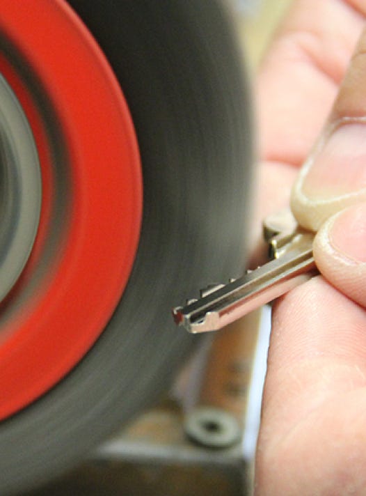 A person holding a key against a spinning grinding wheel.